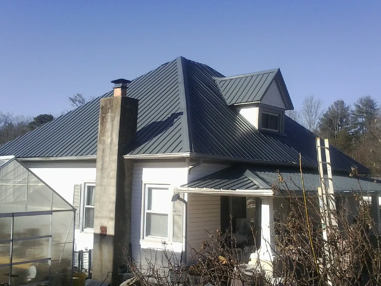 Dark blue standing seam metal roof on a white farmhouse with dormer in Mayville